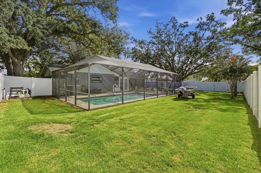 A backyard features a screened-in swimming pool, a small boat on a trailer, and mature trees — 2021 CHARNES DRIVE, LAKELAND, FL