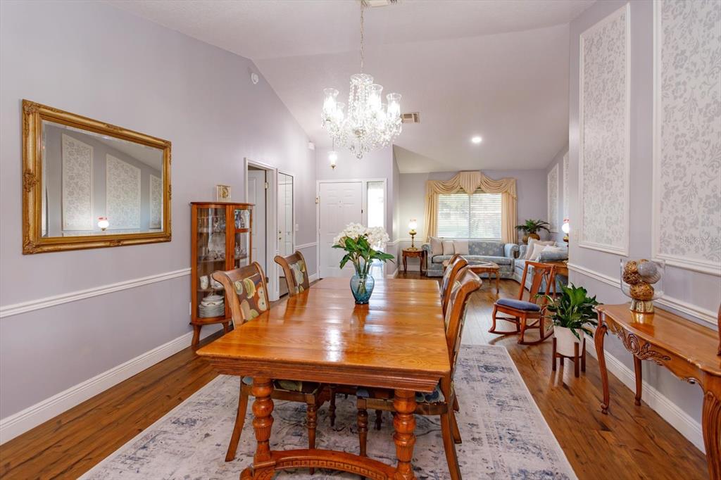 A dining room with a wooden table, chandelier, and adjacent living area with hardwood floors — 9237 SABAL PALM CIRCLE, WINDERMERE, FL