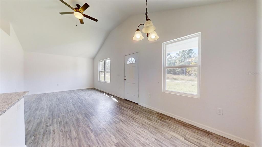 A bright, open-concept living area features vaulted ceilings, light wood-look flooring, and a ceiling fan — 13752 SW 111TH STREET, DUNNELLON, FL