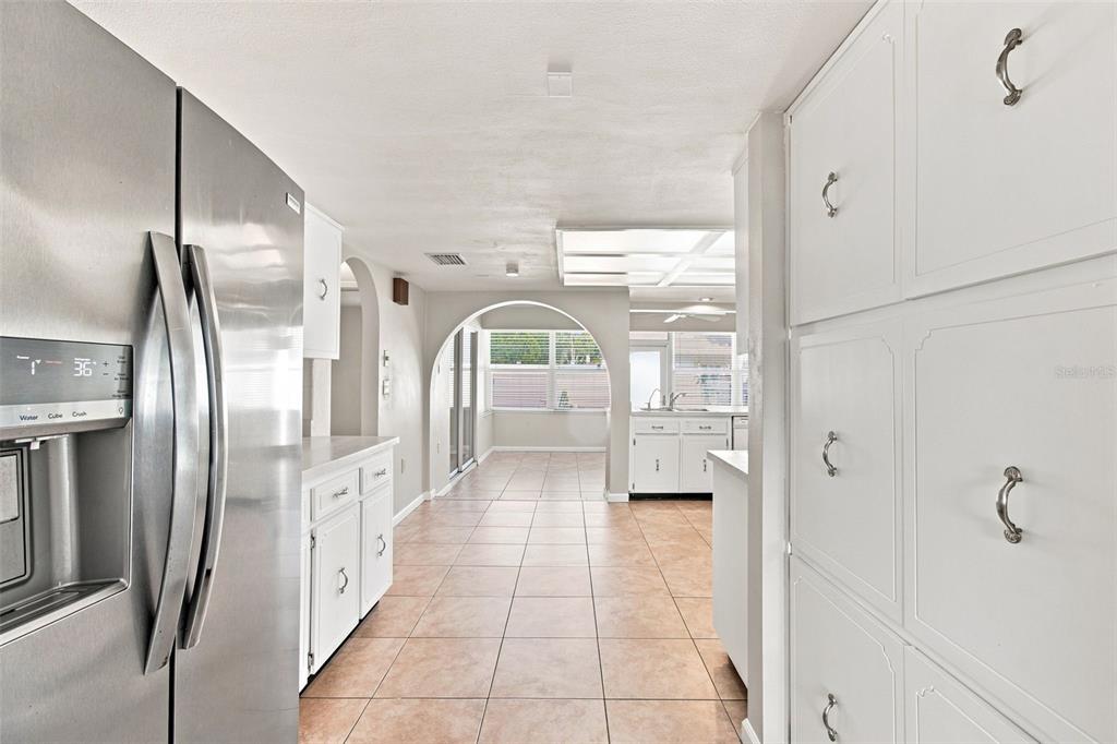 A kitchen with white cabinets, stainless steel appliances, and tile flooring leads to an arched opening — 527 WAYFARER DRIVE, TARPON SPRINGS, FL