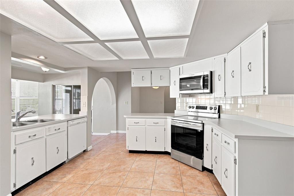 A kitchen with white cabinets, stainless steel appliances, tile flooring, and a grid ceiling light — 527 WAYFARER DRIVE, TARPON SPRINGS, FL