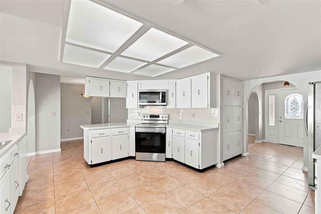 A kitchen with white cabinets, stainless steel appliances, tile flooring, and a large recessed light — 527 WAYFARER DRIVE, TARPON SPRINGS, FL