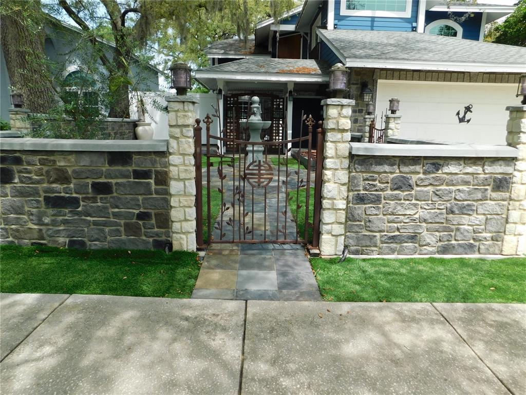 A stone wall with a decorative metal gate leads to the front entrance of a house — 155 MARSHALL STREET, SAFETY HARBOR, FL