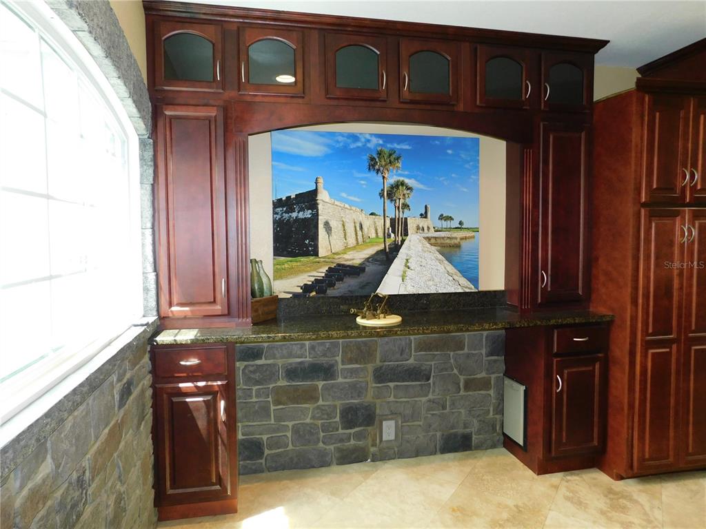 A kitchen wet bar features dark wood cabinetry, stone veneer, and a mural of a fort — 155 MARSHALL STREET, SAFETY HARBOR, FL