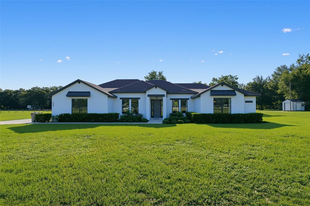 A white, single-story house with a dark roof and black window frames sits on grass — 4650 LAKE PICKETT DRIVE, GROVELAND, FL
