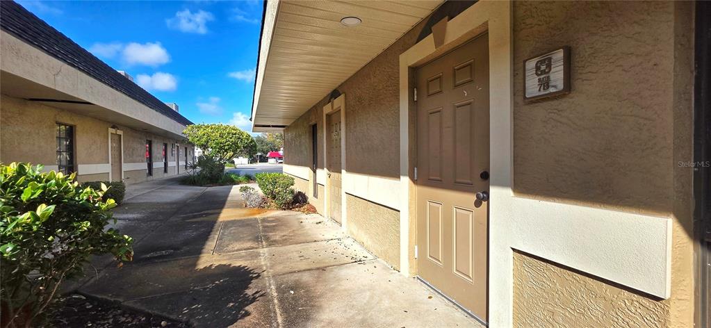 An exterior view of a commercial building with a brown door labeled suite 7B — 2323 CURLEW ROAD UNIT 7B, DUNEDIN, FL
