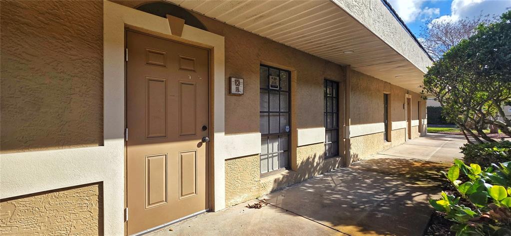 A tan exterior building features a brown door, windows, and a covered concrete walkway — 2323 CURLEW ROAD UNIT 7B, DUNEDIN, FL