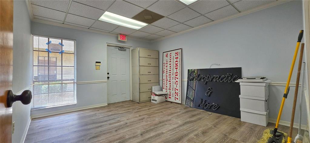 An office room features light blue walls, wood-look flooring, a drop ceiling, and a door — 2323 CURLEW ROAD UNIT 7B, DUNEDIN, FL