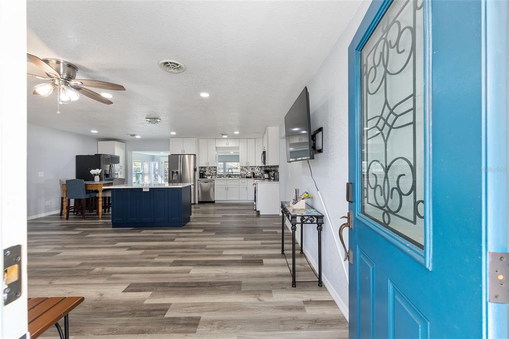 An open-concept kitchen and living area with wood-look flooring, viewed through a blue front door — 10350 SE 43RD COURT, BELLEVIEW, FL