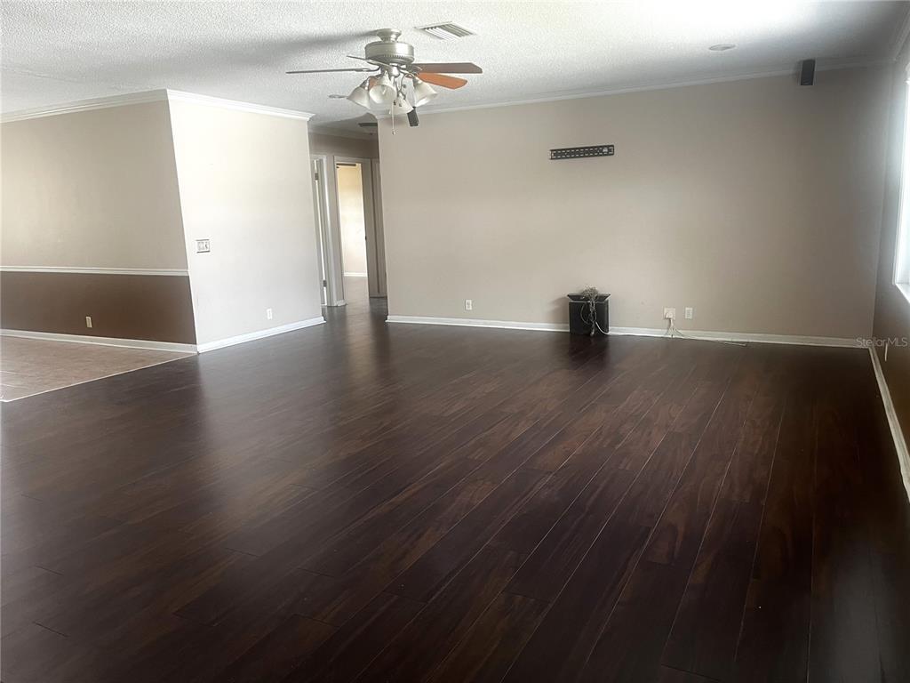 A spacious living room features dark wood flooring, beige walls, and a ceiling fan — 108 LAGOON ROAD, WINTER HAVEN, FL