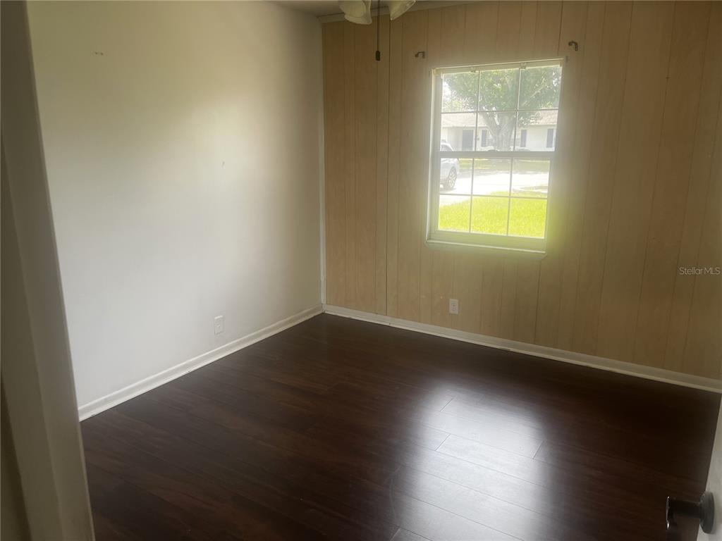 An empty bedroom features dark wood-look flooring, white walls, and one wood-paneled wall — 108 LAGOON ROAD, WINTER HAVEN, FL