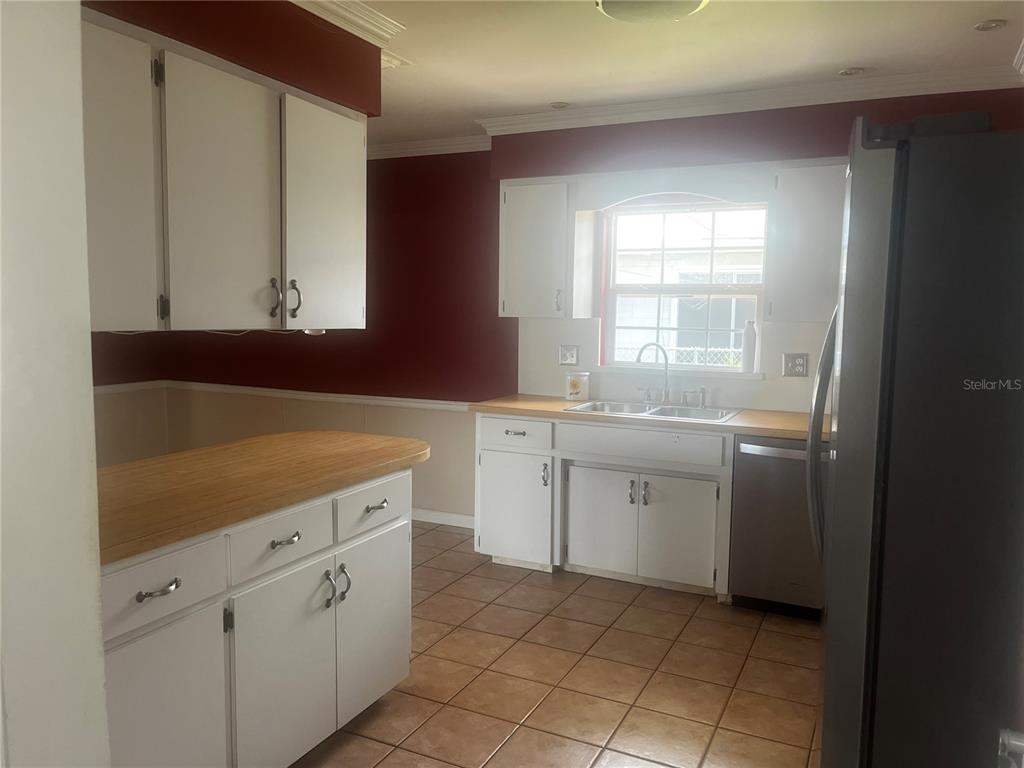 A kitchen features white cabinets, wood countertops, tile flooring, and a black refrigerator — 108 LAGOON ROAD, WINTER HAVEN, FL