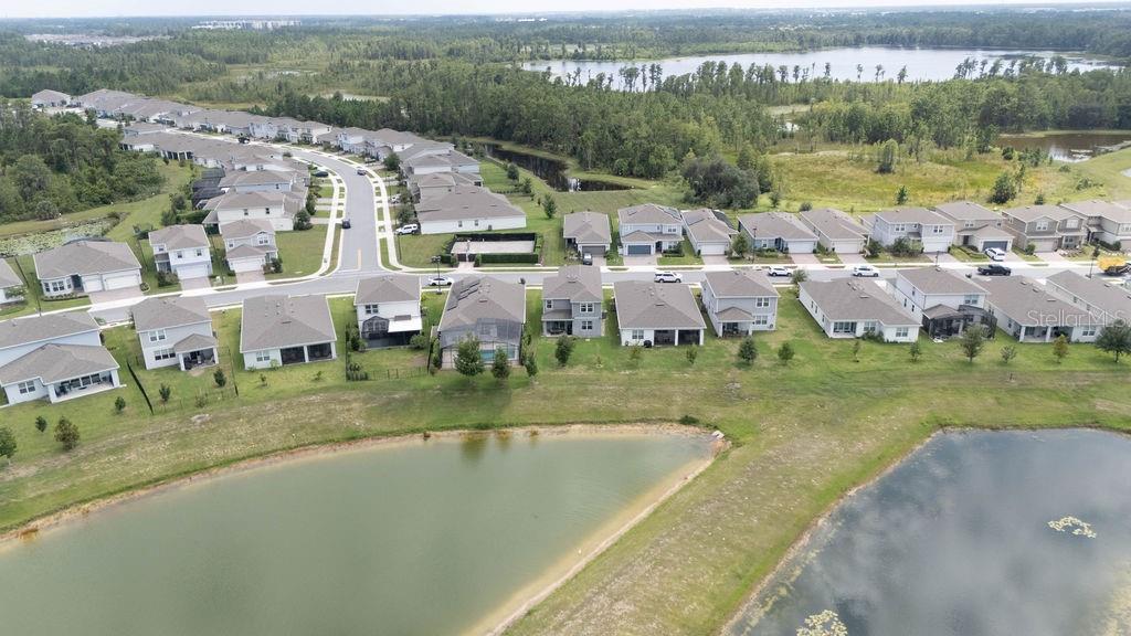 An aerial view shows a suburban neighborhood with houses bordering a pond and forest — 17684 SAW PALMETTO AVENUE, CLERMONT, FL