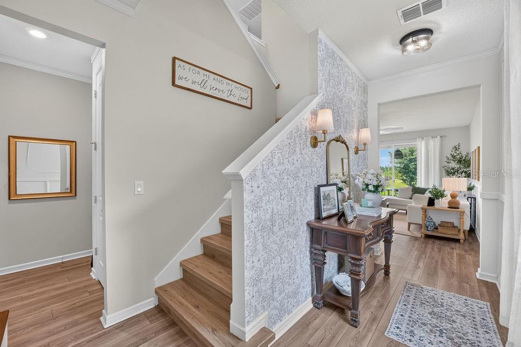 An entryway features a staircase with patterned wallpaper, a wooden console table, and hardwood flooring — 17684 SAW PALMETTO AVENUE, CLERMONT, FL