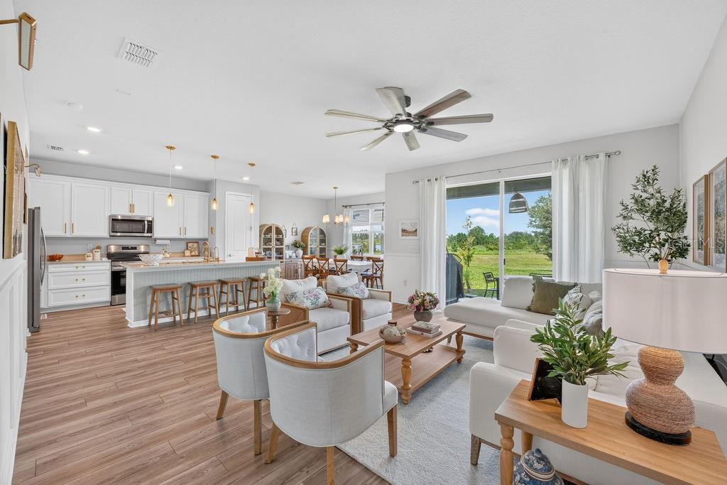 An open-concept living room and kitchen featuring white cabinetry, wood-look flooring, and a sliding door — 17684 SAW PALMETTO AVENUE, CLERMONT, FL