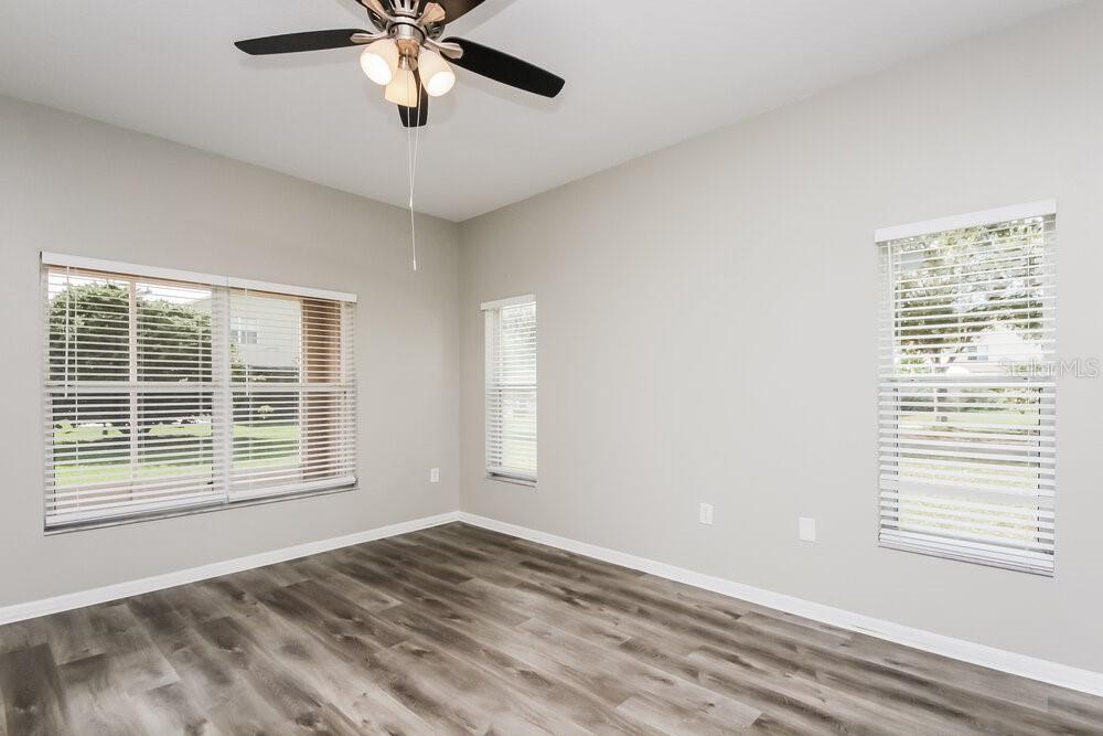 An empty room features light gray walls, wood-look flooring, a ceiling fan, and three windows — 4204 LUGANO COURT, KISSIMMEE, FL