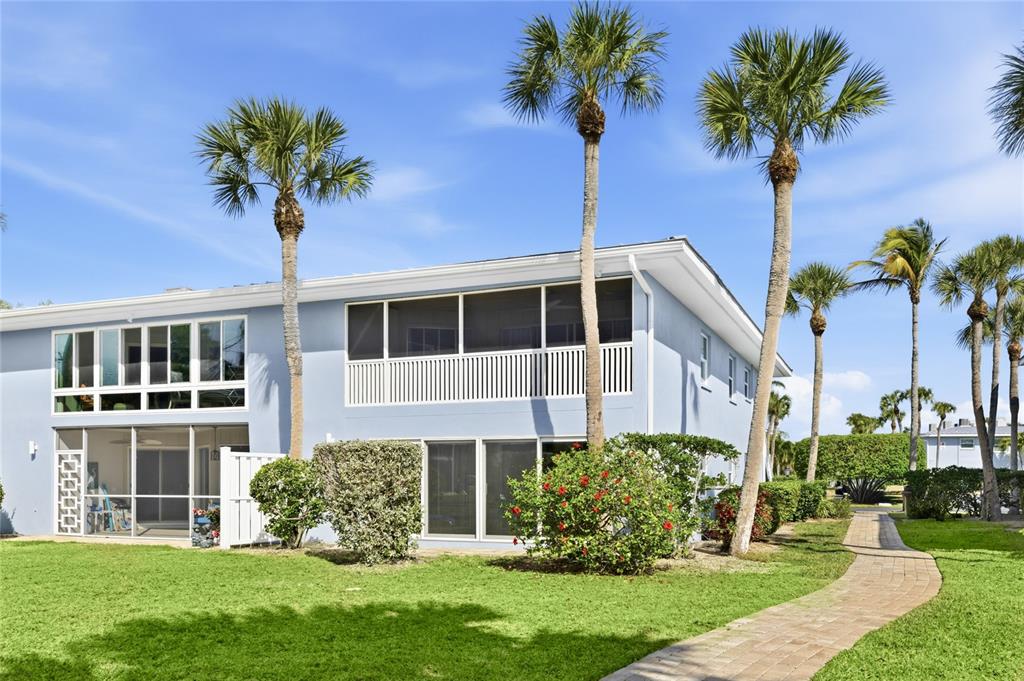 A two-story light blue building with screened balconies and palm trees on a grassy lawn — 600 MANATEE AVENUE UNIT 116, HOLMES BEACH, FL