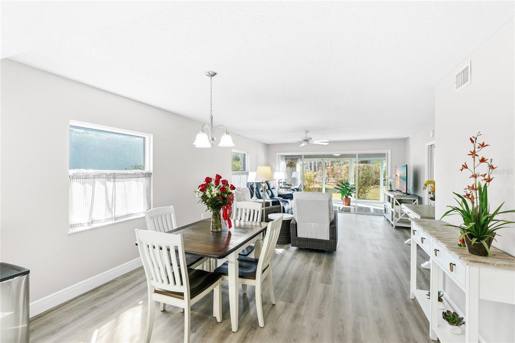 A dining area with a wooden table and chairs opens into a bright living room — 600 MANATEE AVENUE UNIT 116, HOLMES BEACH, FL