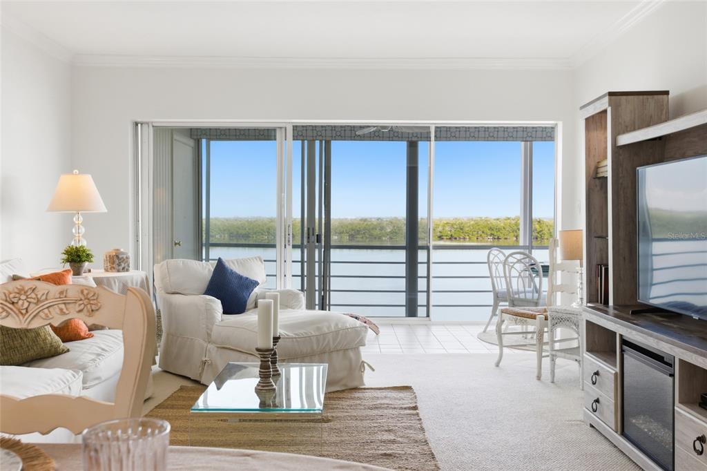 A living room features white furniture, a glass coffee table, and sliding doors overlooking water — 4420 EXETER DRIVE UNIT 303, LONGBOAT KEY, FL