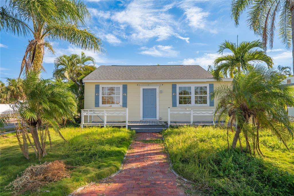 A light yellow single-story house with a blue door, white railings, and a brick walkway — 500 78TH AVENUE, ST PETE BEACH, FL