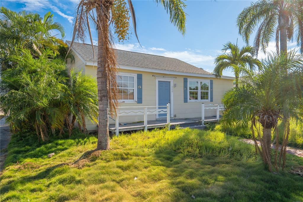 A single-story yellow house with blue shutters and a front porch sits among palm trees — 500 78TH AVENUE, ST PETE BEACH, FL