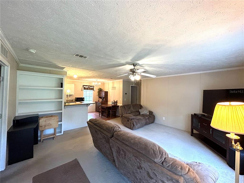 A living room with carpeted floors, a ceiling fan, and an open view to the kitchen — 13191 NE 9TH STREET, WILLISTON, FL