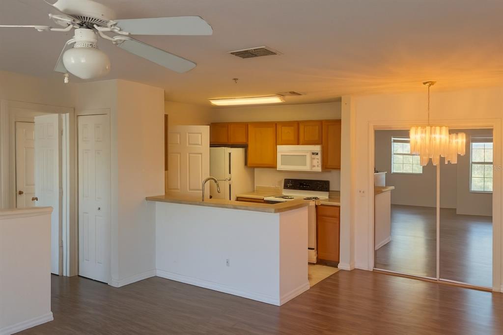 A kitchen with wood cabinets and a breakfast bar overlooks a living area with flooring — 4850 51ST STREET W UNIT 1203, BRADENTON, FL