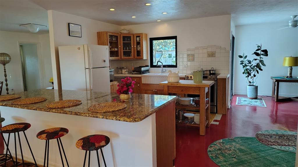 A kitchen features a granite-topped island, wooden cabinets, a white farmhouse sink, and red flooring — 4790 MICHAEL LANE, PONCE INLET, FL