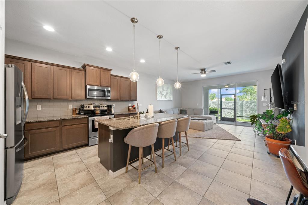 A kitchen with brown cabinets, granite countertops, and an island with three bar stools — 4504 SILVER LINING STREET, SARASOTA, FL