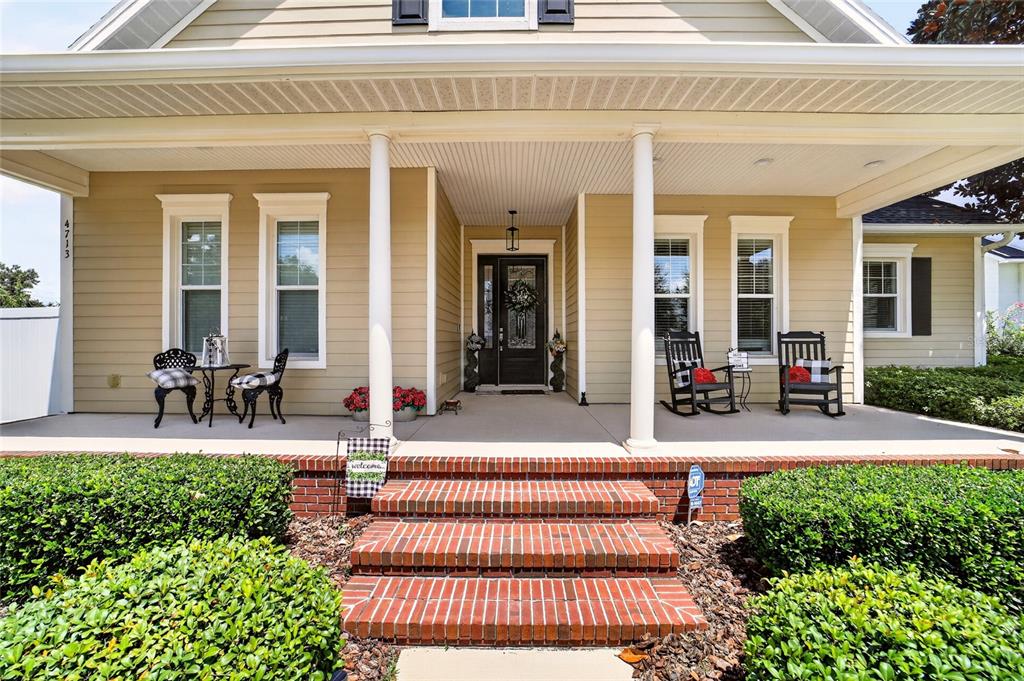 A tan house exterior features a covered front porch with brick steps and rocking chairs — 4713 SE 28TH STREET, OCALA, FL