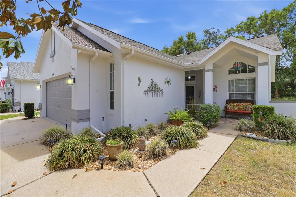 A white single-story house with a two-car garage, front porch, and landscaped garden beds — 3569 S BELGRAVE DRIVE, INVERNESS, FL