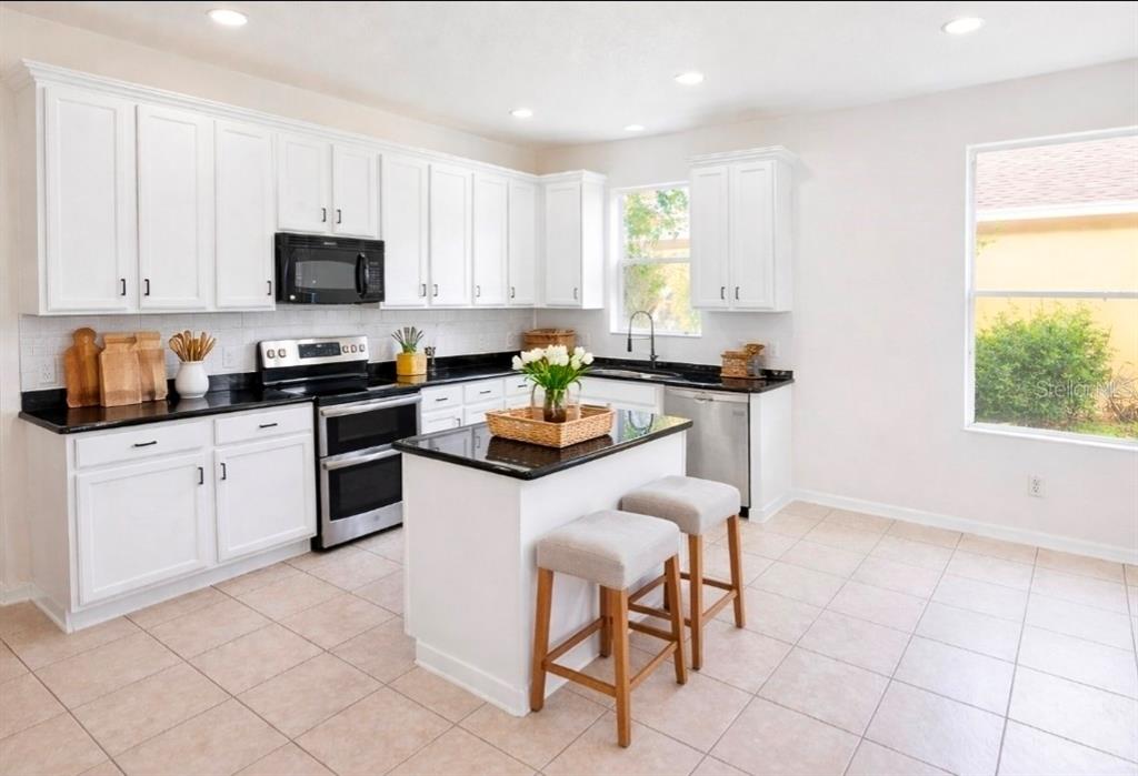 A kitchen features white cabinets, black countertops, a central island with stools, and tile flooring — 1911 WIND MEADOWS DRIVE, BARTOW, FL