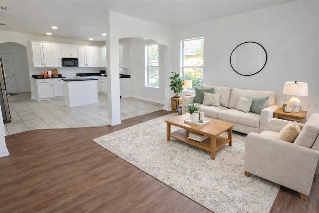 An open-concept living room with wood-look flooring flows into a white kitchen with tile floors — 1911 WIND MEADOWS DRIVE, BARTOW, FL