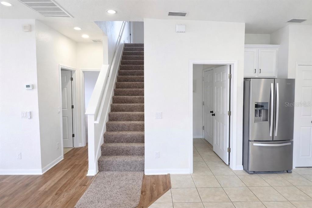 A staircase with brown carpet sits between a wood-floored hallway and a tiled kitchen area — 1911 WIND MEADOWS DRIVE, BARTOW, FL