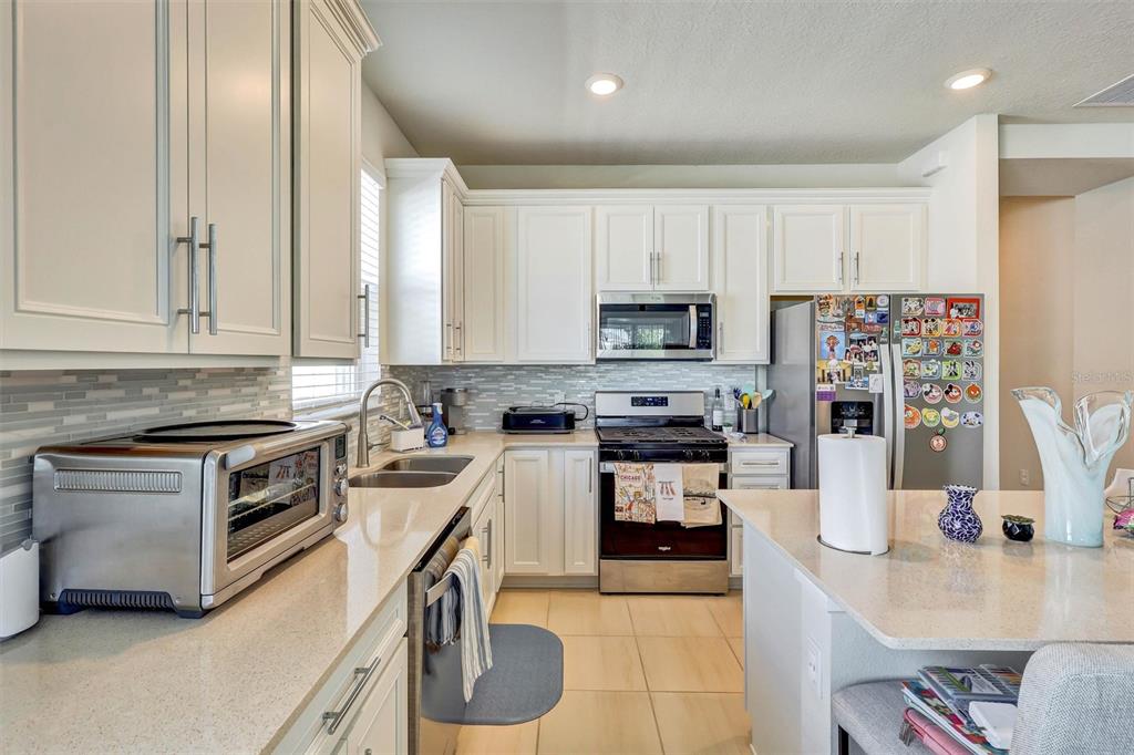 A kitchen features white cabinetry, stainless steel appliances, a tiled backsplash, and a central island — 15806 GEM VIEW ST, WINTER GARDEN, FL
