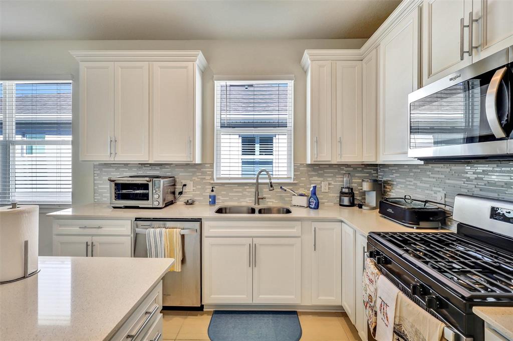 A kitchen with white cabinets, stainless steel appliances, a tiled backsplash, and a double sink — 15806 GEM VIEW ST, WINTER GARDEN, FL