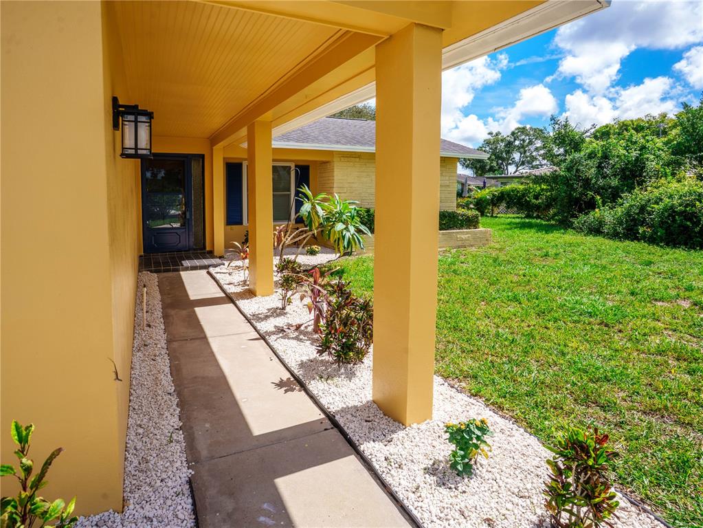 A covered concrete walkway leads to a front door alongside a yellow exterior wall — 1630 BYRNEDALE COURT, PALM HARBOR, FL