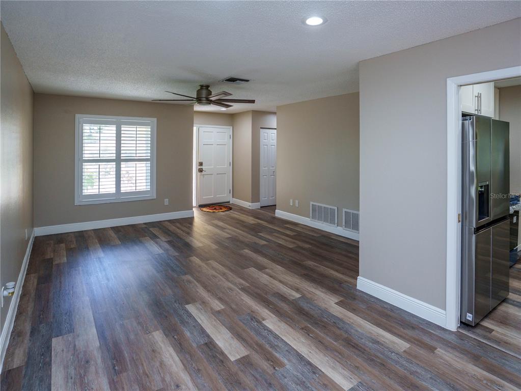 A living room features wood-look flooring, a ceiling fan, and a view of the entryway — 1630 BYRNEDALE COURT, PALM HARBOR, FL