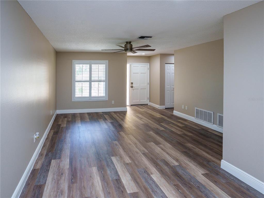 An empty living room features wood-look vinyl flooring, beige walls, a ceiling fan, and a door — 1630 BYRNEDALE COURT, PALM HARBOR, FL