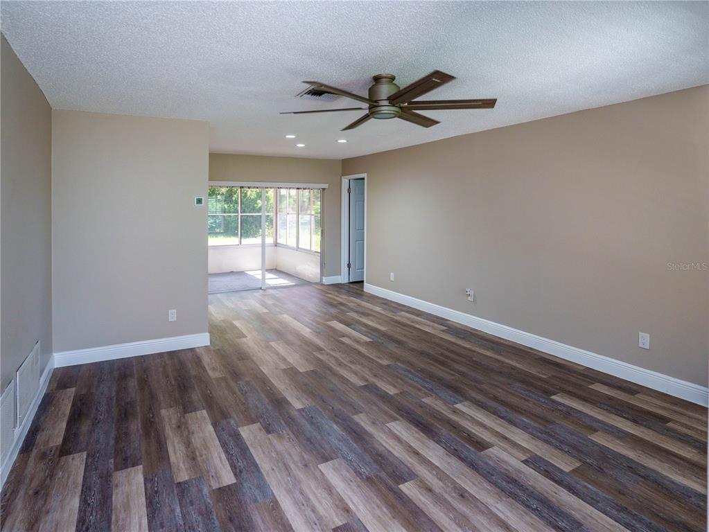 An empty room features wood-look flooring, beige walls, a ceiling fan, and a glass-enclosed porch — 1630 BYRNEDALE COURT, PALM HARBOR, FL