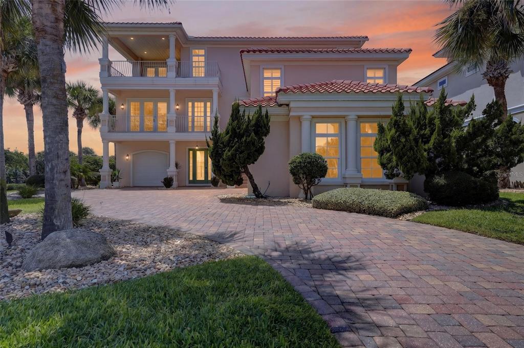 A three-story Mediterranean-style house with a paver driveway, balconies, and a tile roof at sunset — 1 OCEAN RIDGE BOULEVARD N, PALM COAST, FL