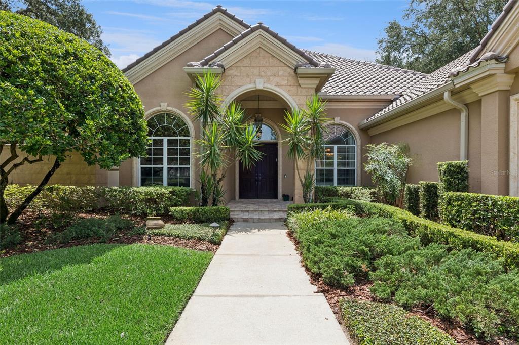 A concrete walkway leads to the arched front entrance of a tan stucco house — 1738 BRACKENHURST PLACE, LAKE MARY, FL