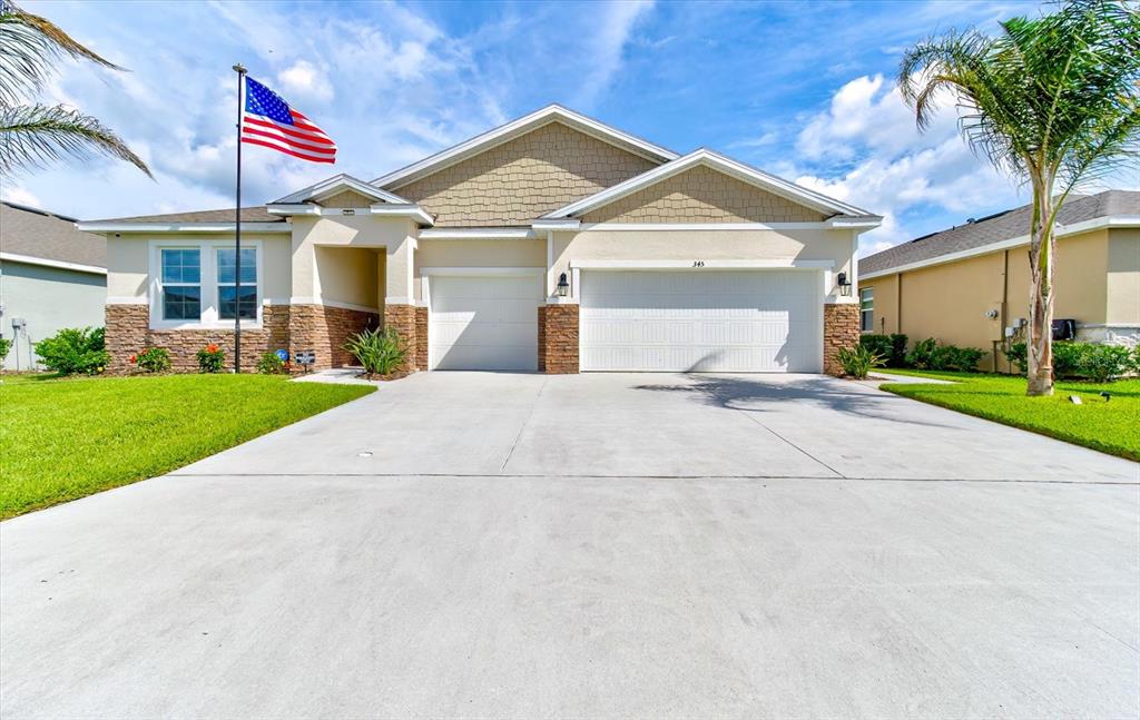 A single-story house with a beige stucco exterior, stone accents, and a three-car garage — 345 E MERIMONT LANE, ORMOND BEACH, FL