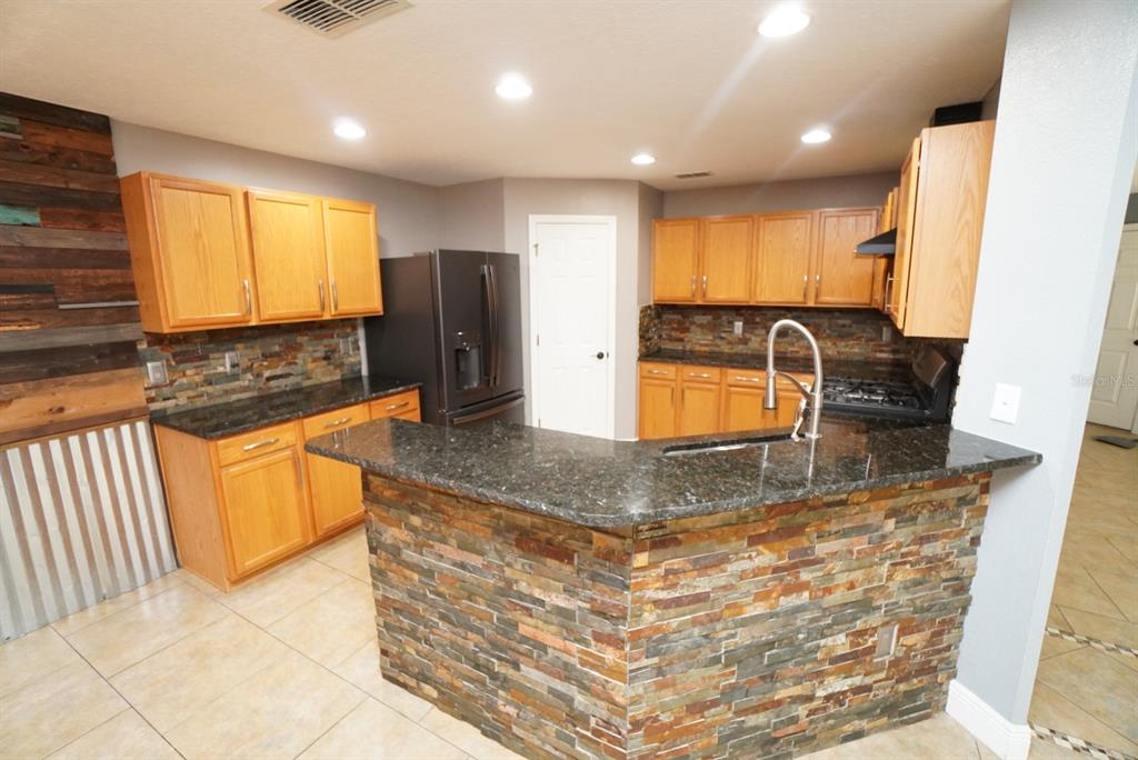 A kitchen features wood cabinets, dark granite countertops, and a stone-tiled breakfast bar — 113 RONA LANE, DAVENPORT, FL