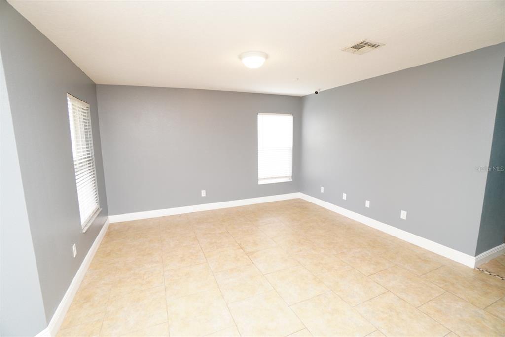 An empty room features gray walls, white trim, tile flooring, and two windows with blinds — 113 RONA LANE, DAVENPORT, FL