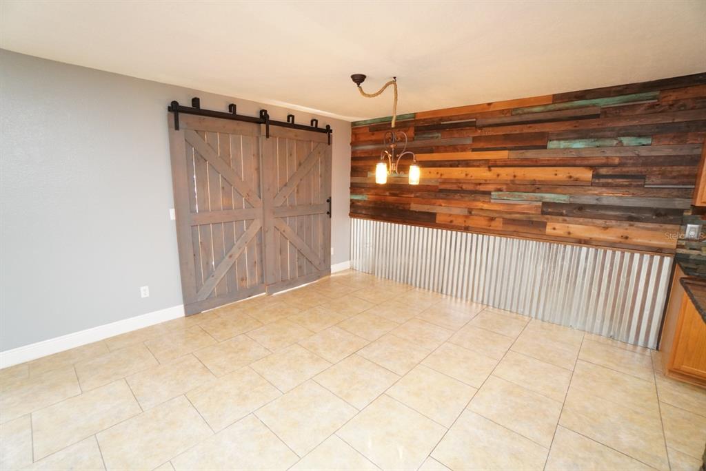 A dining area features tile flooring, a corrugated metal wainscot, wood-plank wall accents, and barn doors — 113 RONA LANE, DAVENPORT, FL