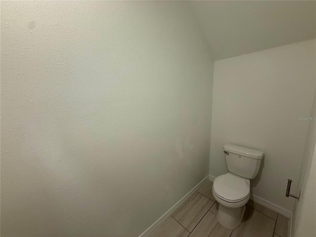 A small bathroom features a white toilet, light-colored tile flooring, and plain white walls — 35190 GRAVELLY DRIVE, ZEPHYRHILLS, FL