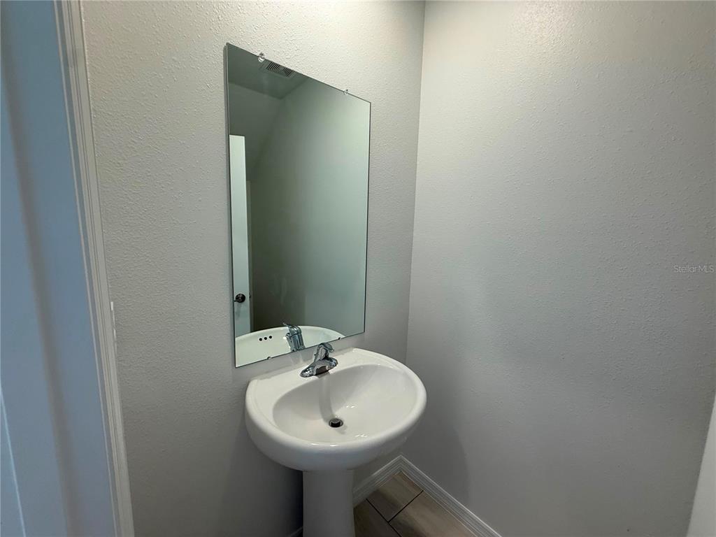 A pedestal sink with a chrome faucet sits below a frameless mirror in a bathroom — 35190 GRAVELLY DRIVE, ZEPHYRHILLS, FL