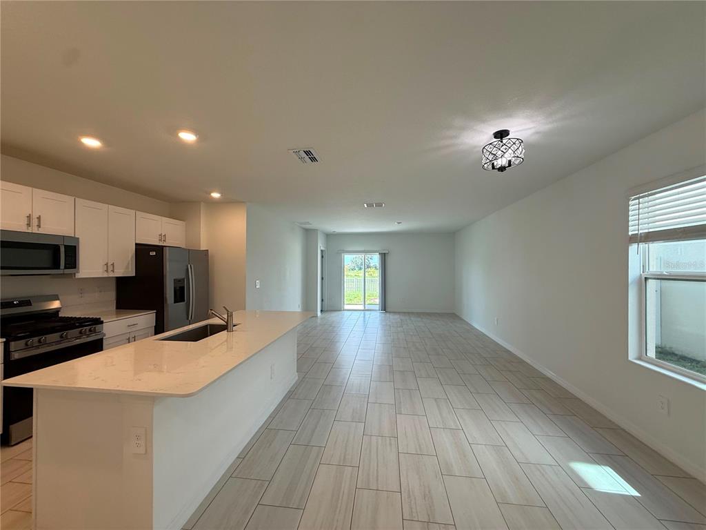 A kitchen with white cabinets and a quartz island overlooks an open-concept living area — 35190 GRAVELLY DRIVE, ZEPHYRHILLS, FL