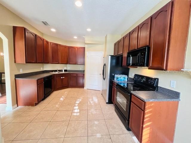 A kitchen features dark wood cabinets, tile flooring, stainless steel appliances, and beige walls — 30 CHIPPENDALE TERRACE, OVIEDO, FL